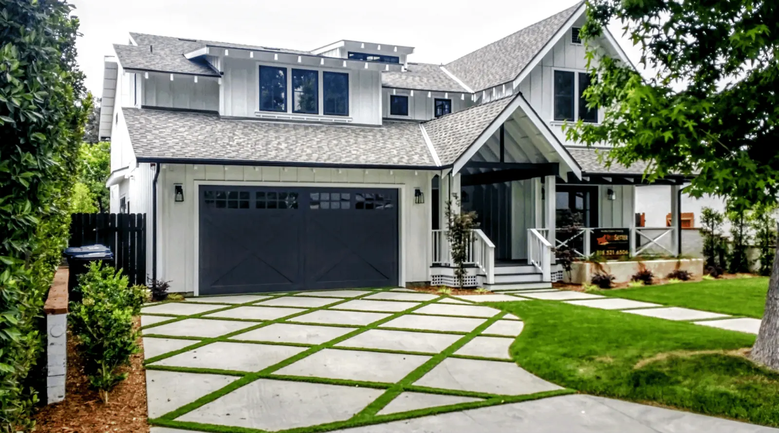 Modern two-story house with gray garage doors, landscaped yard, and geometric driveway design.
